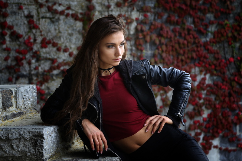 1080P, choker, tanned, wall, brick, hair, three quarter length, sitting, young adult, front view, brown hair, looking away, hairstyle, long hair, leather jackets