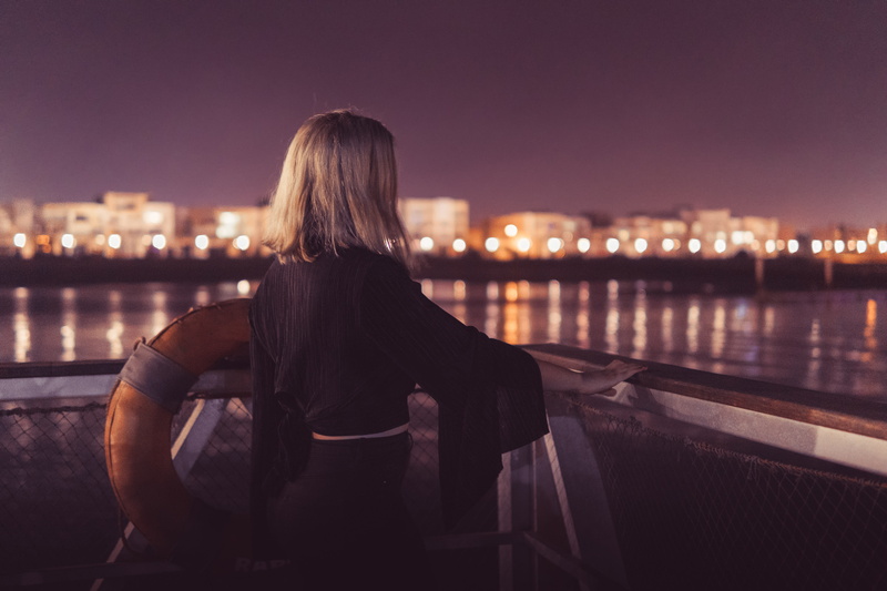 beautiful woman, standing, hairstyle, building exterior, blurred background, cityscape, blond hair, night, built structure, woman, lights, body, hair, water