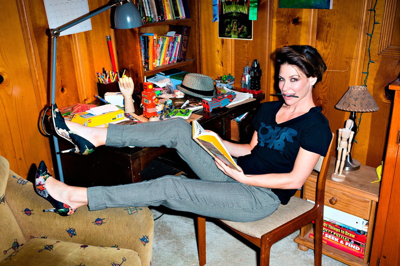 T-shirt, casual clothing, pants, indoors, table, reading, sitting, shirt, leisure activity, wooden surface, adult, neck, high heels, looking at viewer