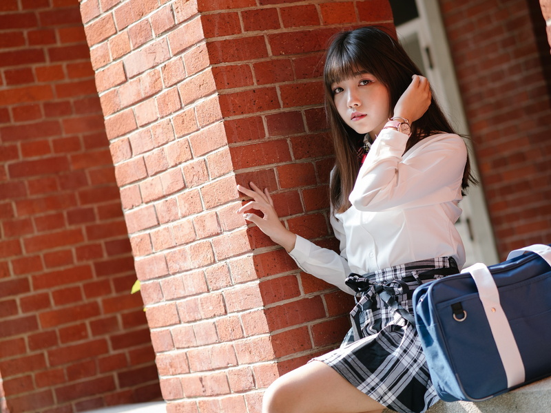 women, brunette, Asian, looking at viewer, 2K, watch, shirt, bow-tie, skirt, handbags, model, sitting, touching hair, women outdoors, bricks