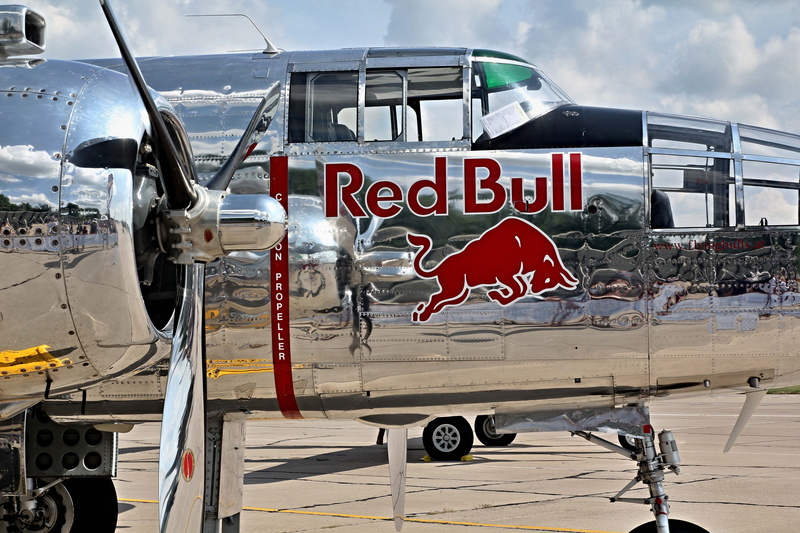 land vehicle, bombarder, car, transportation, day, b25, red bull, airport, nature, no people, aircraft, text, road, historic aircraft, communication, air vehicle