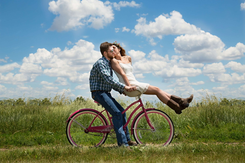 land, real people, happy young couple, emotion, transportation, lifestyles, together, bike, happiness, field, sky, grass, two, two people, couple - relationship