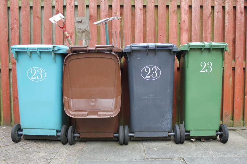 in a row, wheelie, text, plastic, trash can, four, blue, building exterior, recycling bin, metal, taken, rake, wall - building feature, garbage, separation