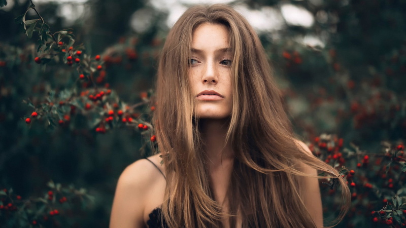 bare shoulders, looking at camera, portrait, depth of field, plants, freckles, tree, focus on foreground, headshot, windy, one person, hair in face, front view