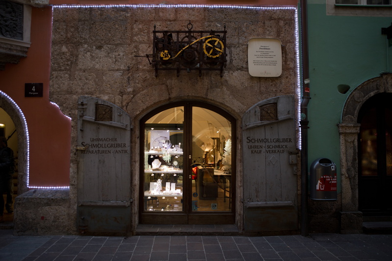 non-western script, western script, watchmaker, door, outdoors, footpath, no people, tiled floor, arch, building exterior, night, christmas lights, text