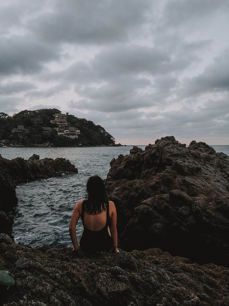 cliff, sky, woman, shoreline, one person, lifestyles, wearing, rock - object, person, 2K, outdoors, leisure activities, water, promontory, apparel, solid