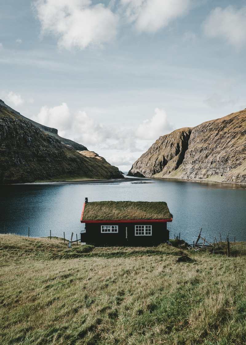 sky, built structure, cloud - sky, no people, grass, plant, brown, text, lake, mountain range, mountain, house, clouds, saksun, water, outdoors, cabin