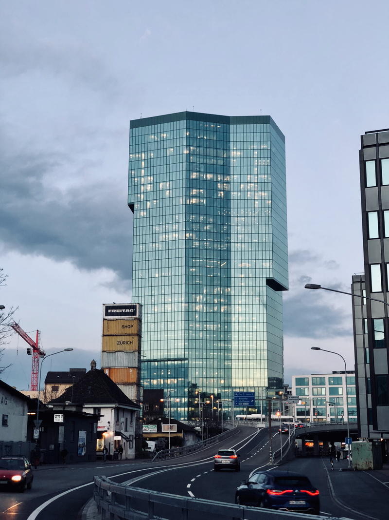 building, sky, land vehicle, prime tower, car, dusk, tower, architecture, office building exterior, sign, skyscraper, mode of transportation, outdoors