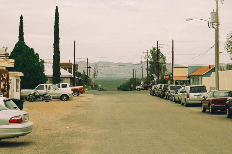buildings, cars, town, direction, gray, vehicles, city, tree, houses, trees, car, building exterior, stationary, posts, clouds, mountains, city street