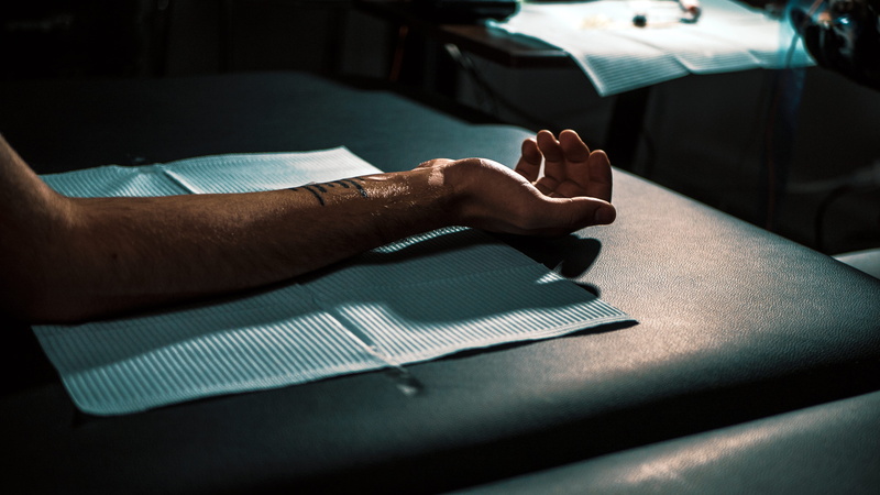 lying down, transportation, one person, adult, person, palm up, dark, social issues, shadow, human limb, tattooing, fore arm, tattoo artist, barefoot, table