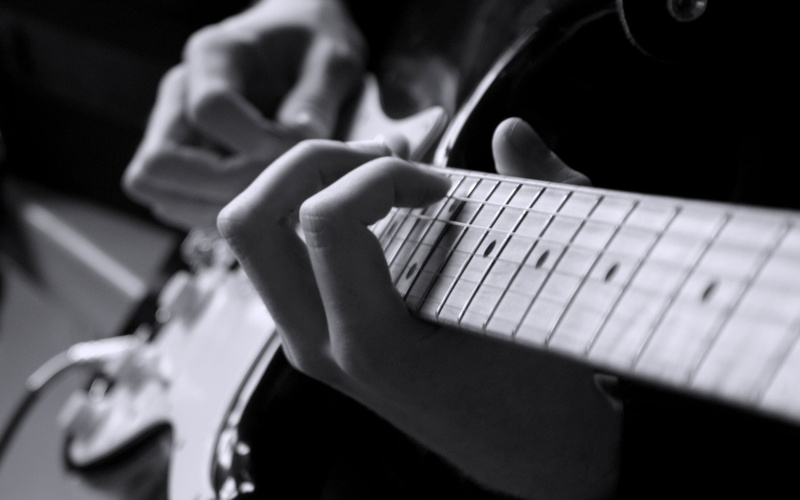plucking an instrument, human body part, music, selective focus, six-string electronic guitar, electric, close-up, black background, focus on foreground