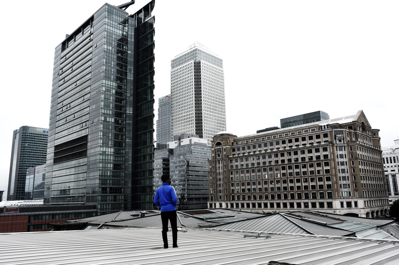 city life, built structure, office, 5K, outdoor, skyline, clear sky, modern, standing, real people, roof, one person, building exterior, urban, man, full length