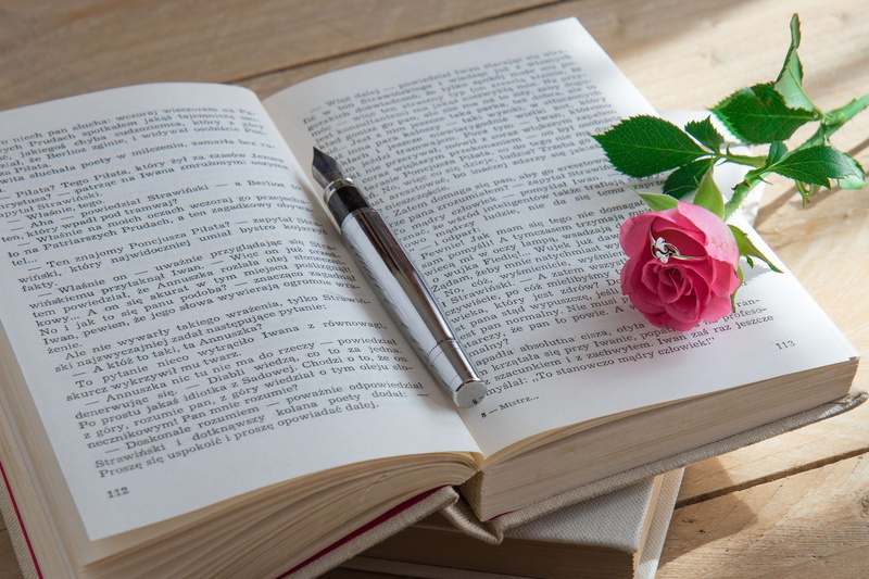 literature, love story, indoors, high angle view, ring, wooden background, textbook, close-up, flower, western script, paper, no people, romantic scene