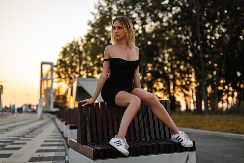 model, sneakers, blonde, dress, depth of field, cleavage, sunset, black dress, women, bare shoulders, 2K, Olga Belaya, looking away, necklace, outdoors
