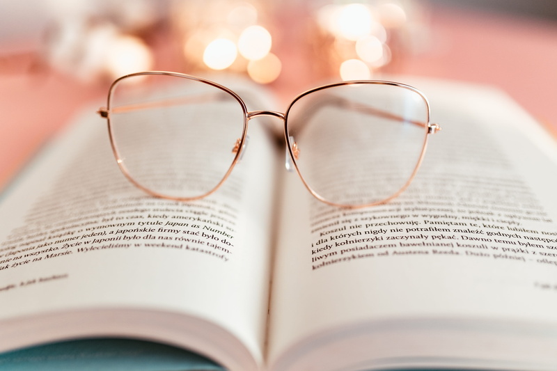pink backgound, selective focus, still life, text, glasses, two objects, publication, indoors, studio shot, eyewear, personal accessory, focus on foreground