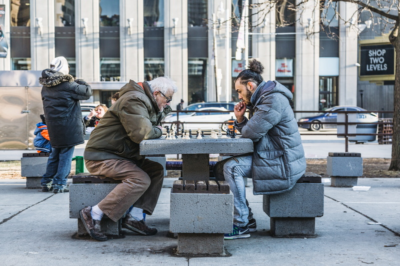 outdoors, 5K, building exterior, architecture, adult, board game, real people, windows, reflection, chess, seat, city, sitting, social issues, male, winter