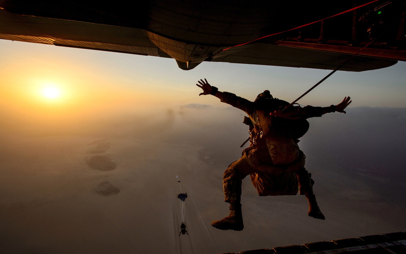 full length, one person, arms outstretched, desert, leisure activity, outdoors, human arm, parachutes, jumping, water, lifestyles, paratroopers, sky, mid-air