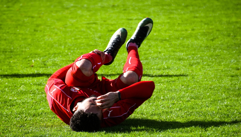 uniform, plant, nature, real people, young, full length, adult, shadow, football player, day, knee, green color, injury, sportswear, man, one person, lying down