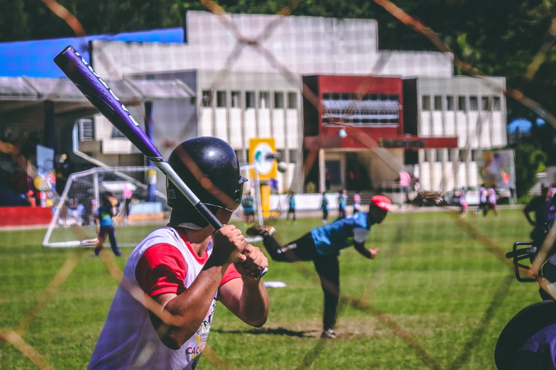 uniform, wear, helmet, sport, grass, athletes, standing, ball, holding, nature, players, focus on foreground, incidental people, baseball cap, clothing