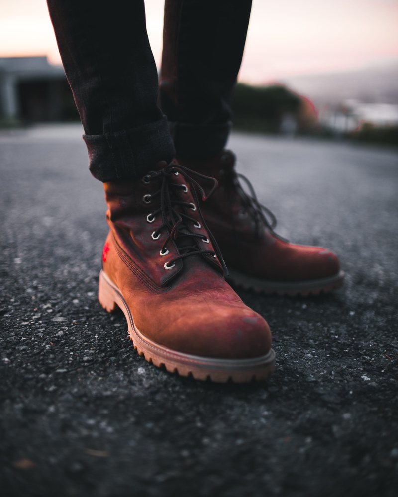 wearing, human limb, ground, one person, blur, walk, sneakers, boot, fashion, body part, selective focus, adventure, sunset, black, close-up, road, standing