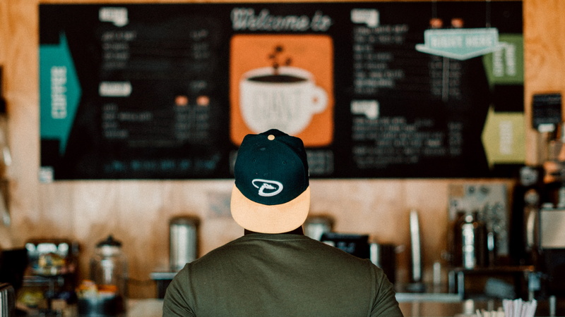 coffee shop, clothing, back, standing, hat, unrecognizable person, casual clothing, menu, man, photo, disguise, business, obscured face, view, shop, board