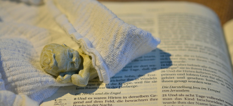 jesus birth, selective focus, text, christ, publication, angle, bible, indoors, close-up, figure, santon, focus on foreground, human body part, diaper