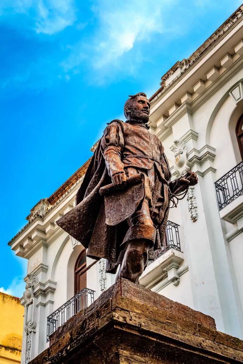 city, sculpture, art and craft, building exterior, 5K, male likeness, building, sky, day, representation, rusty, human representation, outdoors, travel