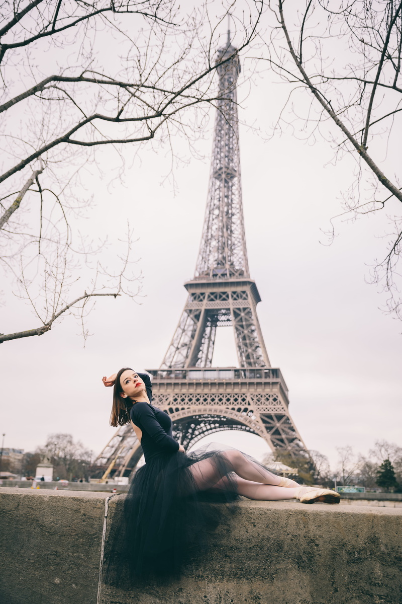 black dress, sky, hairstyle, young adult, sitting, monument, posing, plant, one person, tree, france, leisure activity, background, tower, woman, built structure
