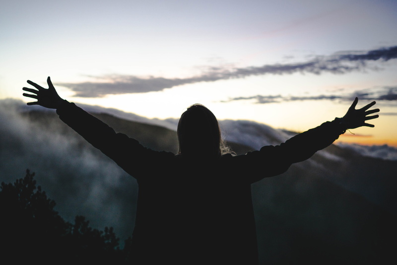 arms raised, waist up, adventure, rear view, freedom, prayer, mountain, light, one person, leisure activity, sunlight, human arm, real people, sky, flare