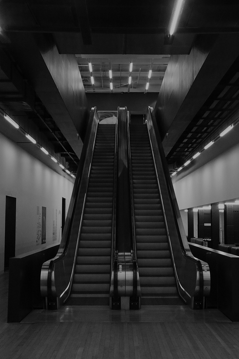 interior, railing, escalator, banister, grayscale, building, lighting, real people, underpass, corridor, flooring, low angle view, black and white, stairs