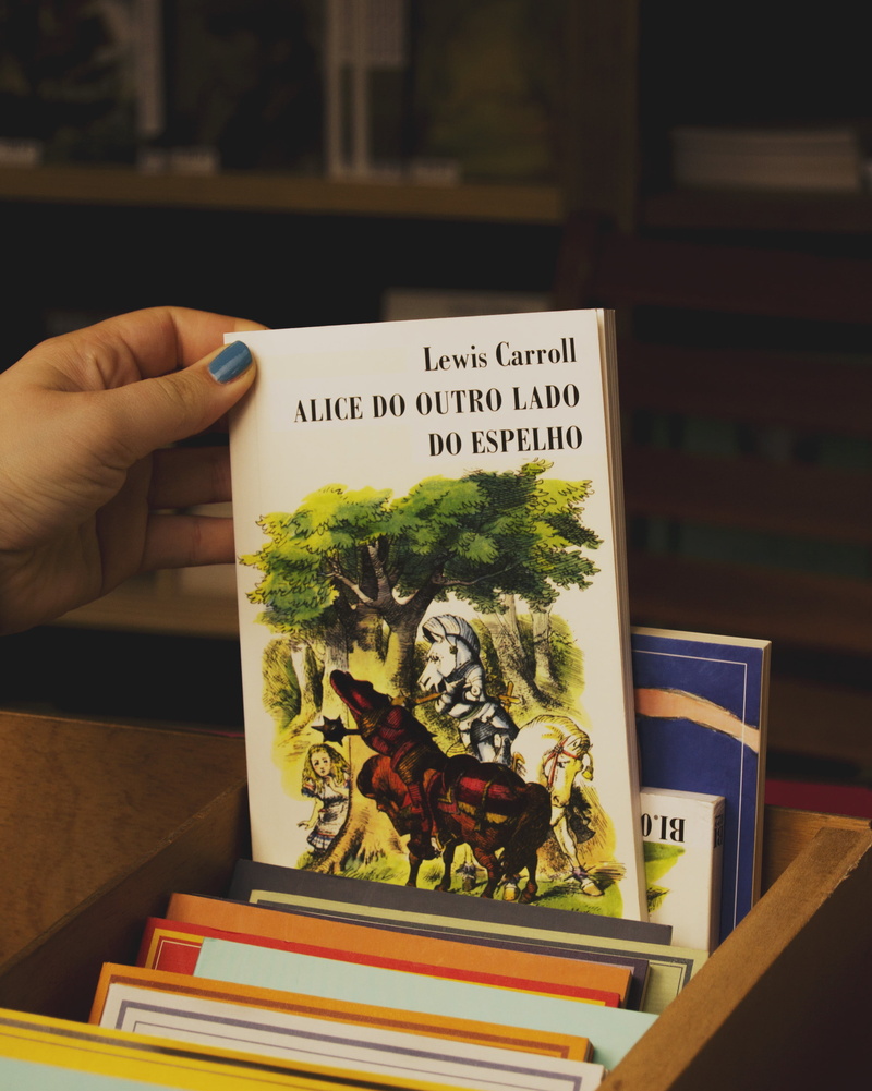 one person, book, holding, 2K, finger, text, book cover, communication, body part, education, indoors, western script, real people, lifestyles, Alice in Wonderland