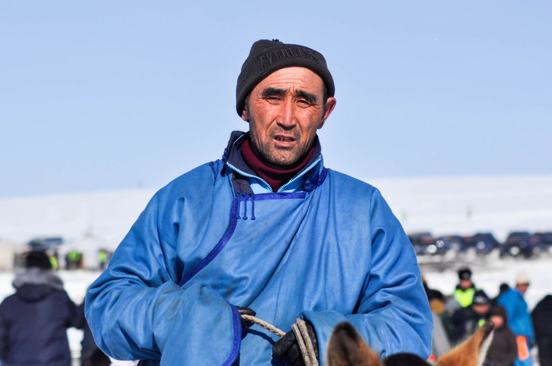 looking at camera, 2K, one person, waist up, incidental people, mature men, day, man, traditional cloth, grassland, focus on foreground, copy space, winter