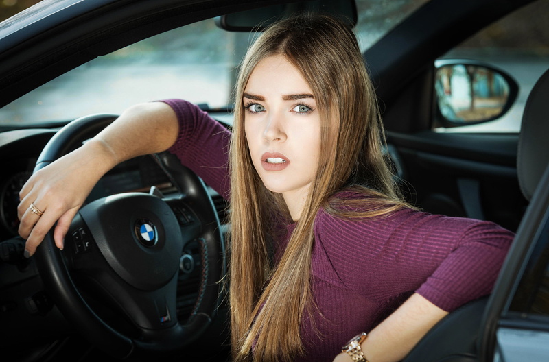 inside a car, BMW, sweater, women with cars, long hair, vehicle interior, headshot, looking at camera, leisure activity, sitting, outdoors, one person