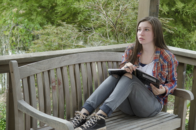 Enid, sitting, leisure activity, plant, casual clothing, hairstyle, one person, outdoors, adult, Katelyn Nacon, lifestyles, real people, full length, bench