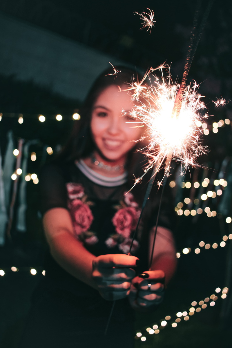 outdoors, sparks, flash, sparkler, motion, firecrackers, front view, smiling, long exposure, standing, dark, light, real people, colors, lights, woman