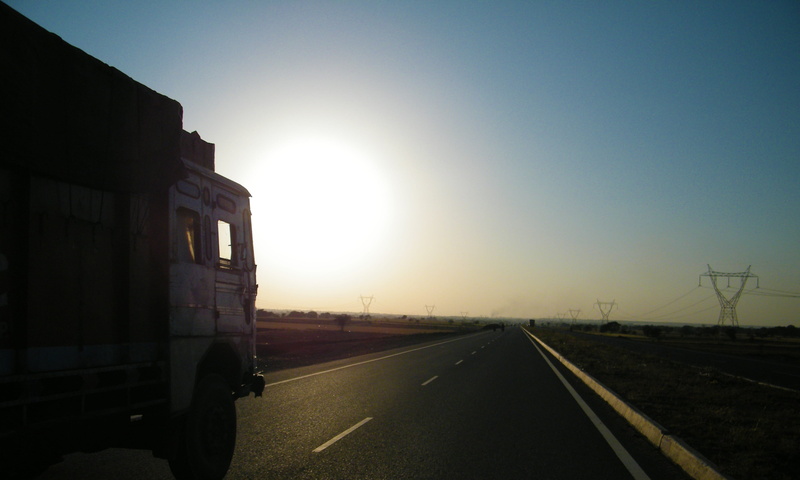 street, land vehicle, road marking, truck, clear sky, moving, sky, architecture, road, road trip, sunset, sunbeam, no people, box, sunlight, towards, asphalt
