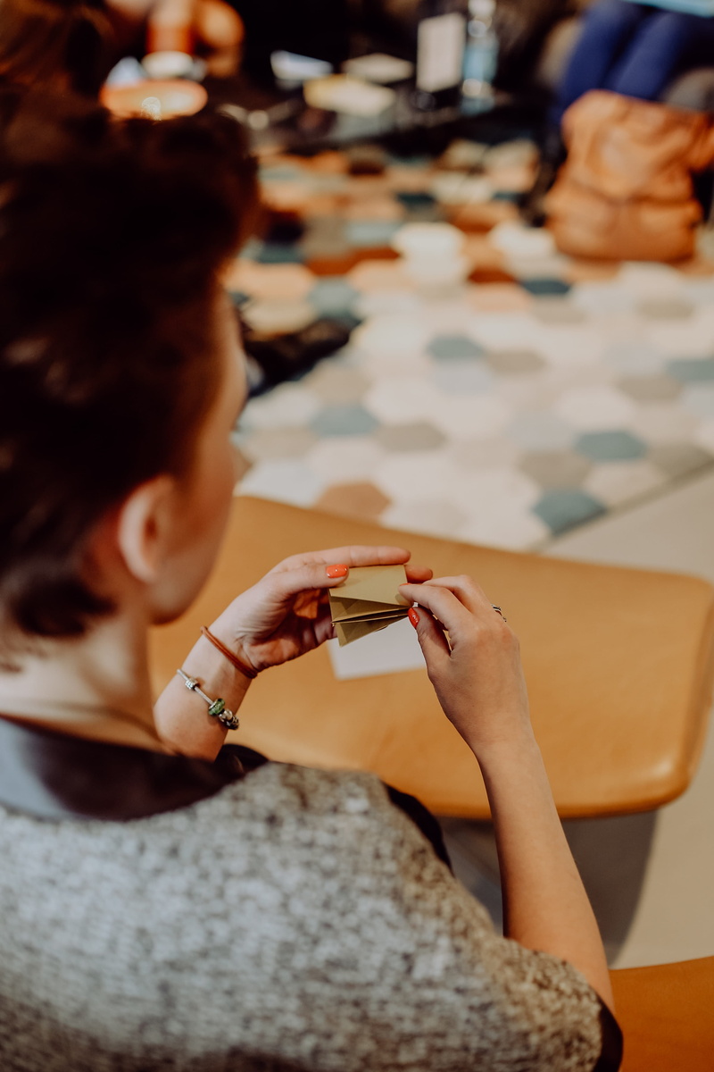 table, holding, artwork, one person, craft, hand, women, making, sitting, origami, folding, casual clothing, adult, indoors, paper, focus on foreground