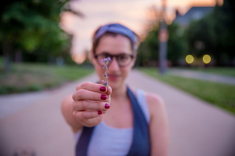 field, woman, glasses, smile, casual clothing, purple, eye, adult, portrait, focus on foreground, person, plant, head, sunset, hand, glass, human, depth