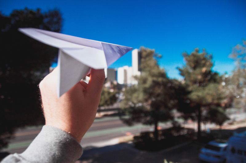 day, hand, paper plane, plane, car, fold, transportation, view, city, outdoors, blue, bush, finger, holding, building exterior, airplane, tree, site seeing