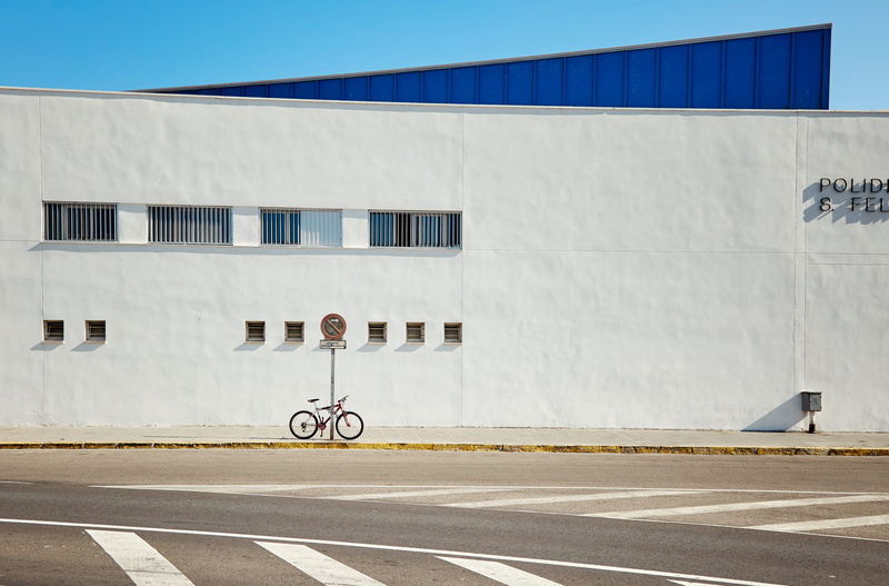 wall, built structure, white, land vehicle, road marking, spain, outdoors, road, blue, street, minimal, day, symbol, mode of transportation, bike, single