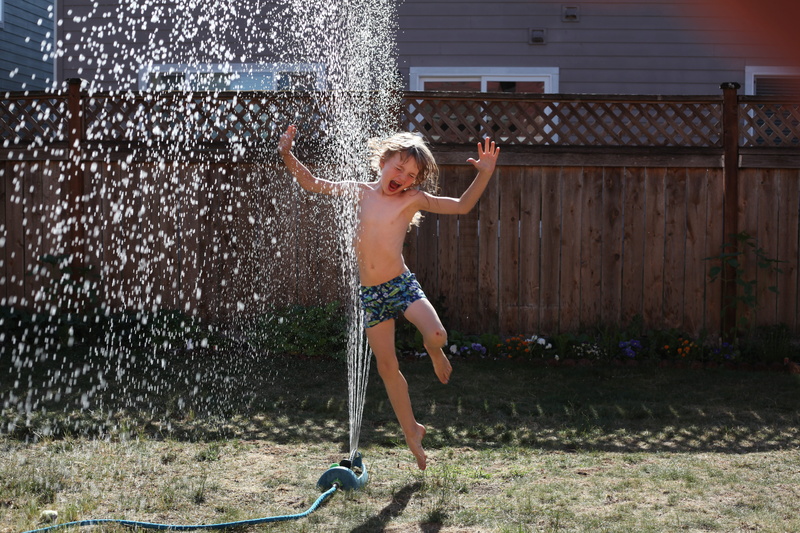 one person, little, facial expression, body part, full length, arms raised, childhood, nature, daylight, motion, young, swimwear, sprinkler, fun, emotion