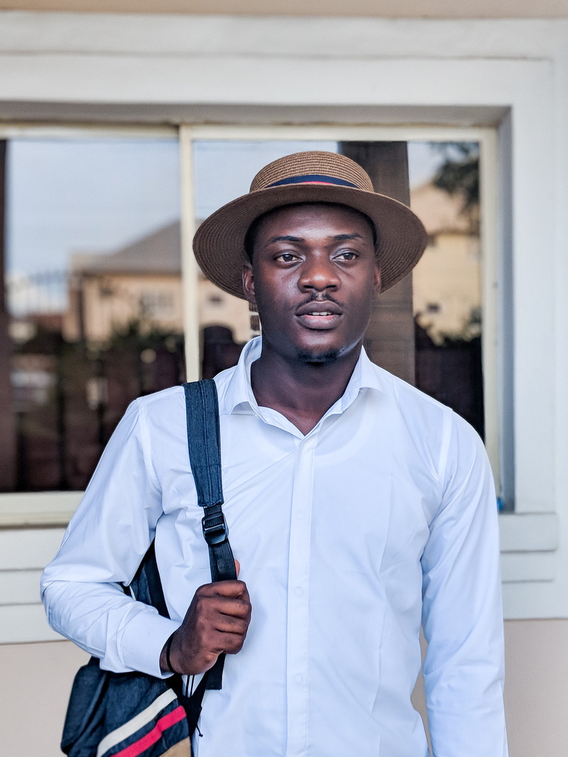 young men, building exterior, portrait, standing, face, 2K, young adult, looking at camera, lagos, carrying, igbo, shirt, hat, lifestyles, leisure activity