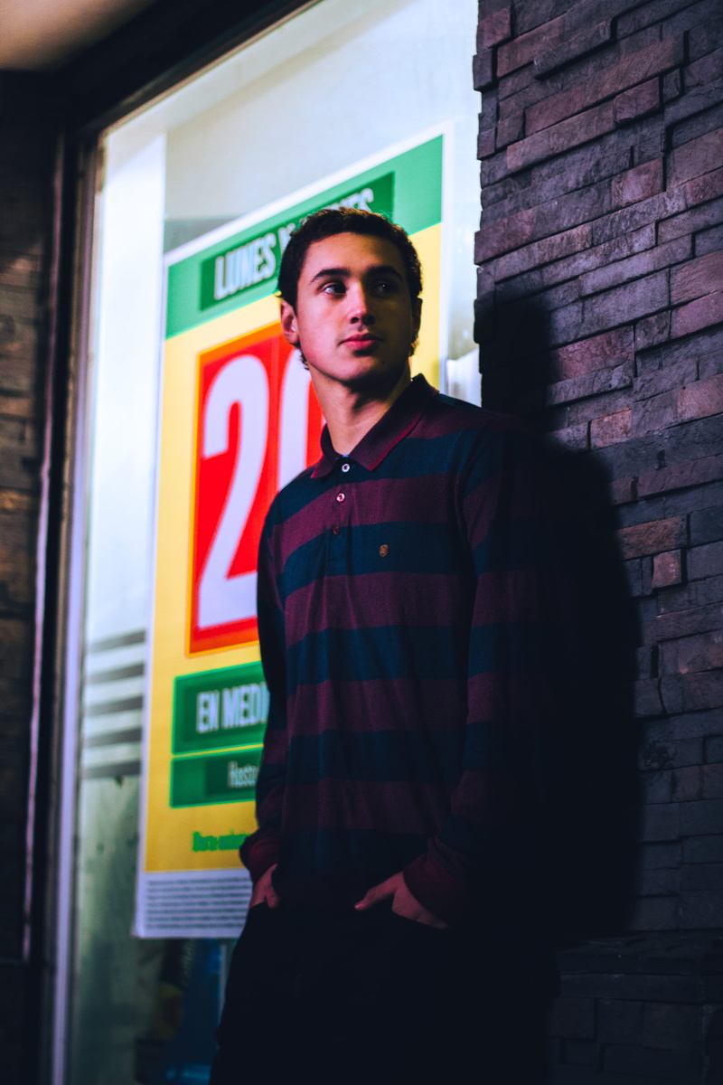 leisure activity, shirt, brick, wearing, street, looking away, wear, man, building exterior, hands in pockets, young men, leaning, offense, actor, contemplation