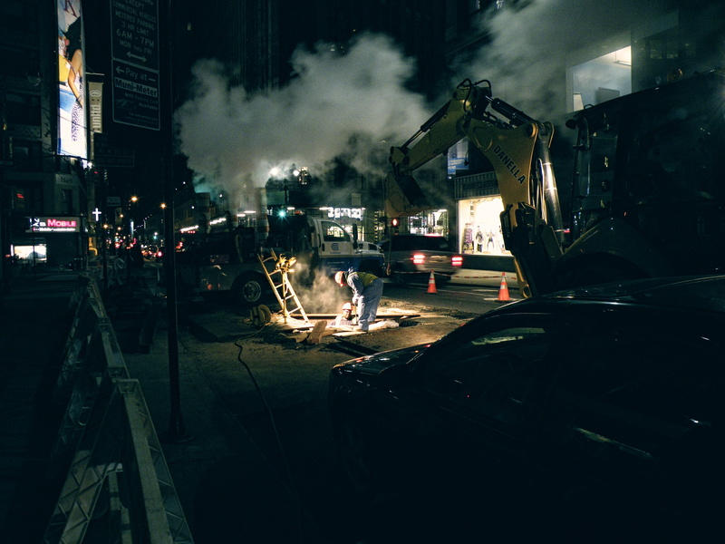 worker, loader, car, traffic cone, crane, real people, smoke - physical structure, nighttime, road, mode of transportation, architecture, pollution, construction