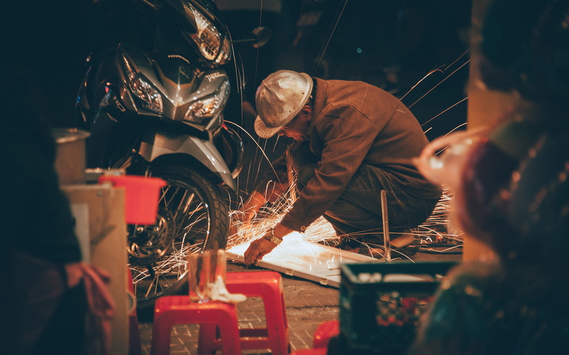 front, motorcycle, grinder, two people, repairing, man, focus on background, photography, spark, real people, selective focus, 4K, brown, metal industry