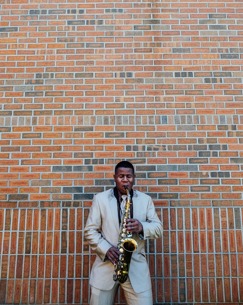 building, jacket, music, men, brick, adult, mature adult, standing, musician, smiling, near, bricked, person, looking at camera, male, suit, front, musical instrument