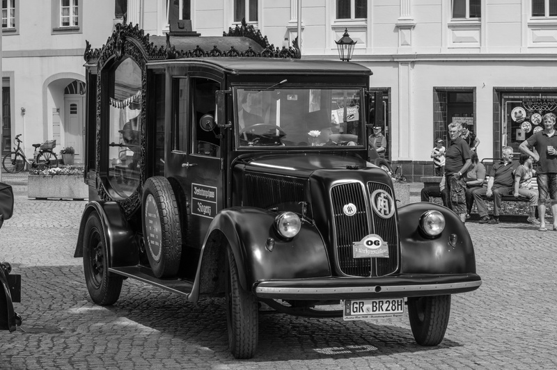 building, incidental people, day, outdoors, hearse, funeral, automotive, vintage car, street, motor vehicle, oldtimer, mode of transportation, commercial vehicle