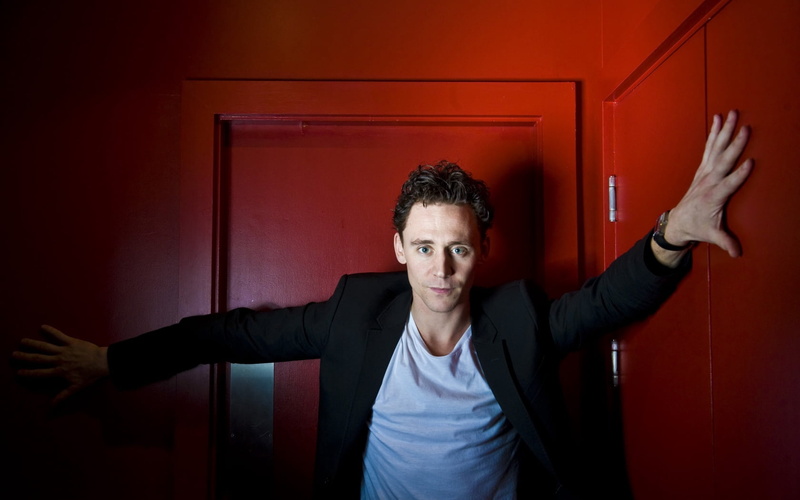 tom hiddleston, front view, human limb, smiling, waist up, 720P, looking at camera, black, actor, indoors, hairstyle, standing, body part, photoshoot