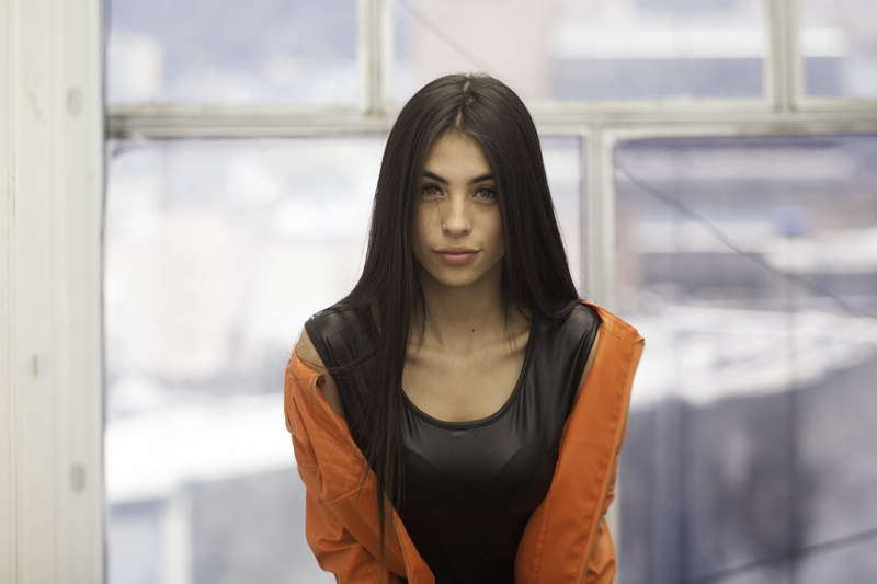 orange jacket, long hair, looking at viewer, hair, adult, outdoors, model, jacket, women, focus on foreground, day, glass - material, women indoors, beautiful woman