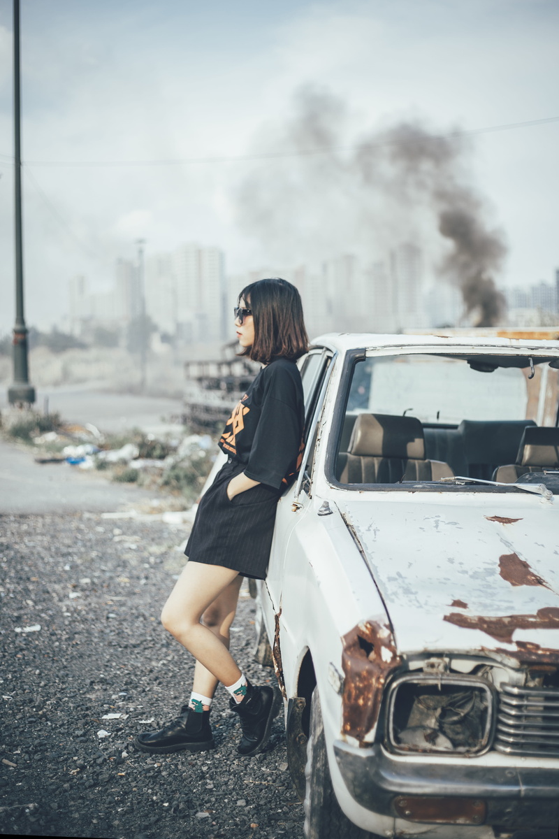woman, building exterior, adult, broken, mode of transportation, classic car, wearing, outdoors, architecture, daylight, car, land vehicle, rusty, vehicle